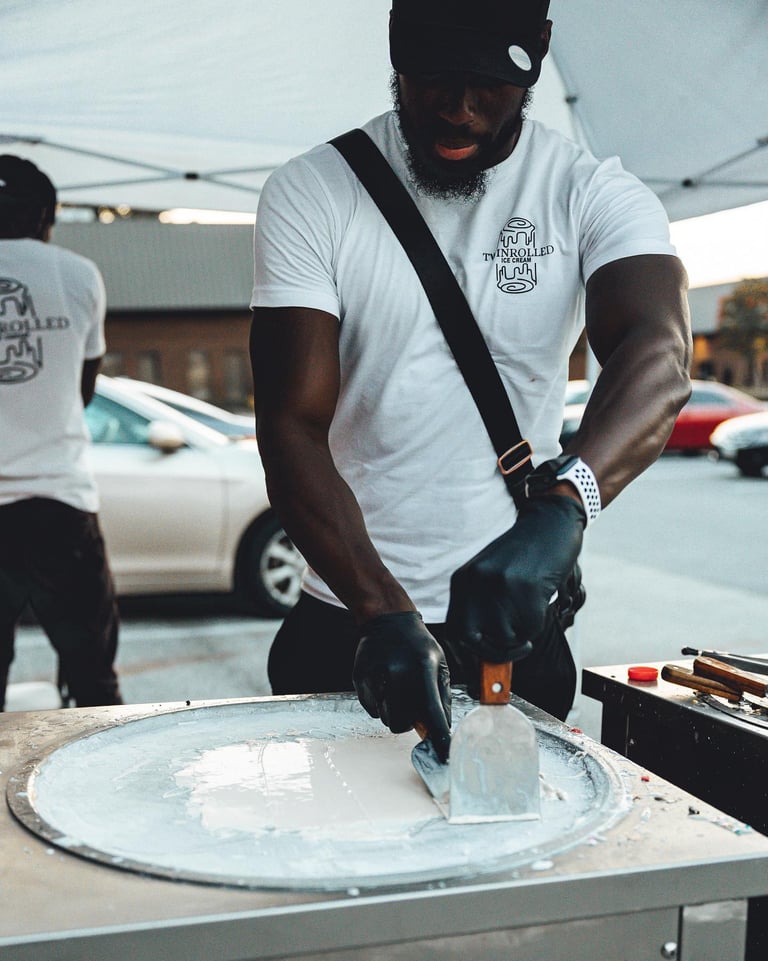 Man in white t-shirt and black cap working on a car wheel, wearing black gloves while working outdoors in a parking lot